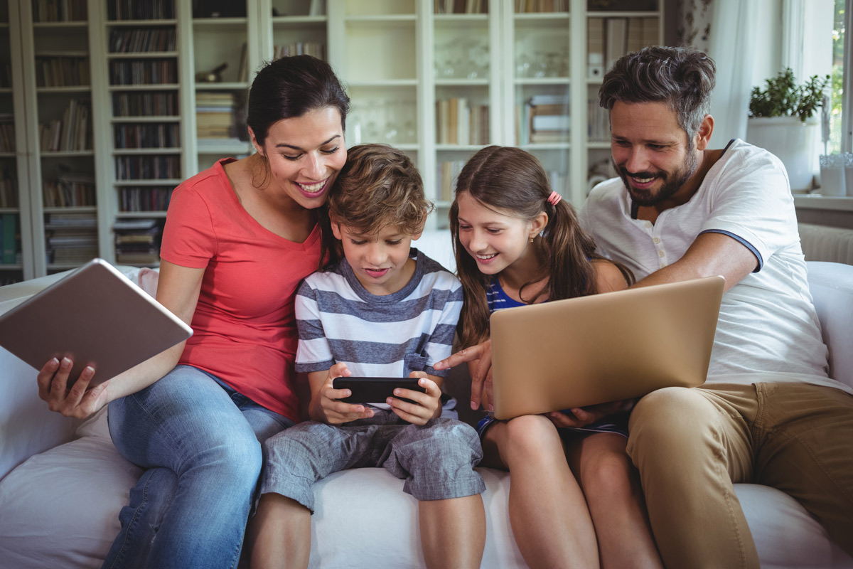 Eine Familie sitzt auf der Couch mit Tablet, Laptop und Handy in der Hand. 