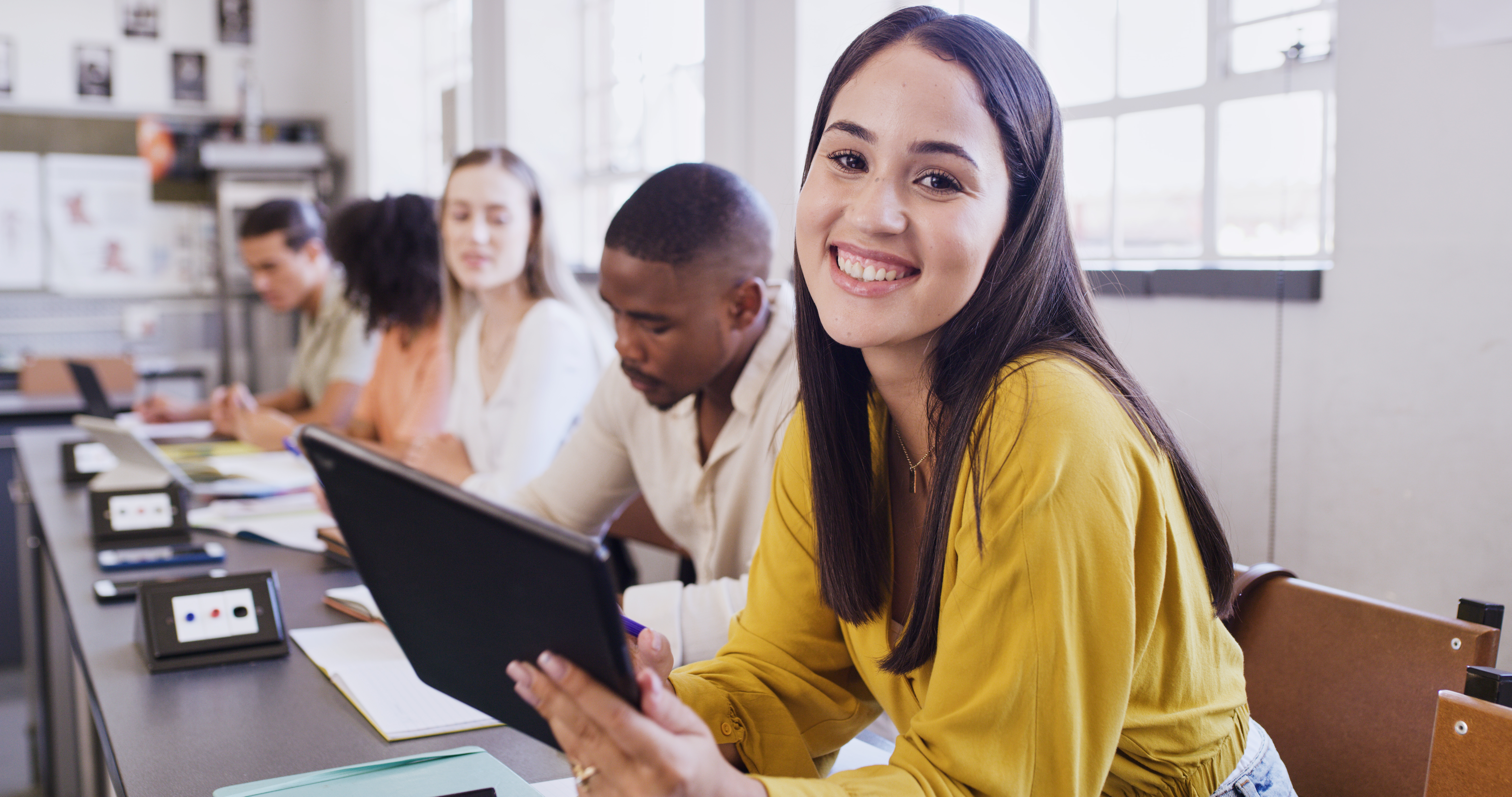 Eine junge Frau lacht mit einem Tablet in der Hand. Sie schaut einen an. 