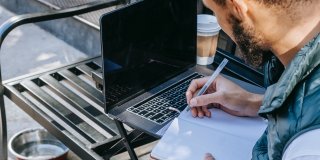 Foto eines Mannes, der in einem Café mit Laptop arbeitet