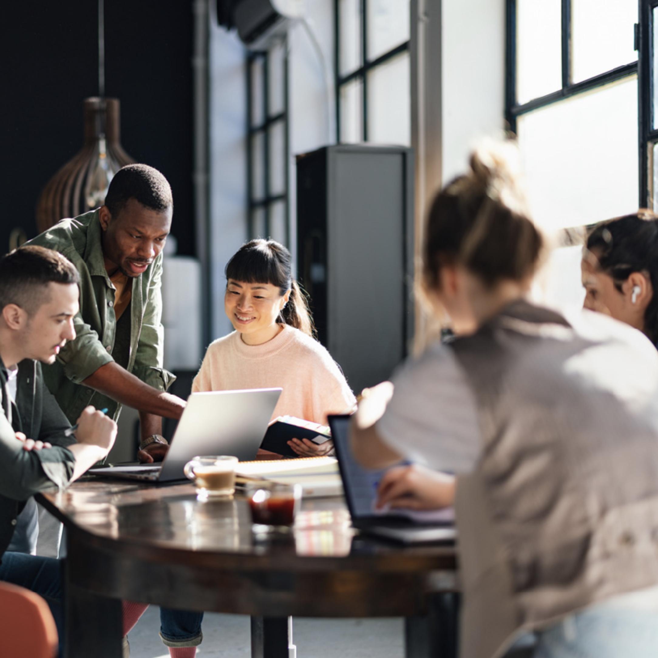 Eine Gruppe an Menschen sitzen am Tisch vor Laptops