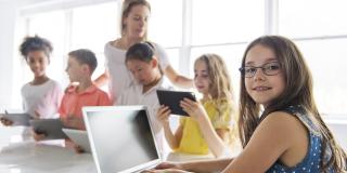 Junges Mädchen im Klassenzimmer vor einem Laptop, die sich zu einem dreht. 